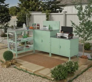 A mint green outdoor kitchen cabinet set with a grill and storage units in a garden patio area
